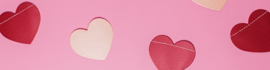 Alla hjärtans dagpyssel med pappershjärtan i rött och rosa, placerade på en rosa bakgrund.